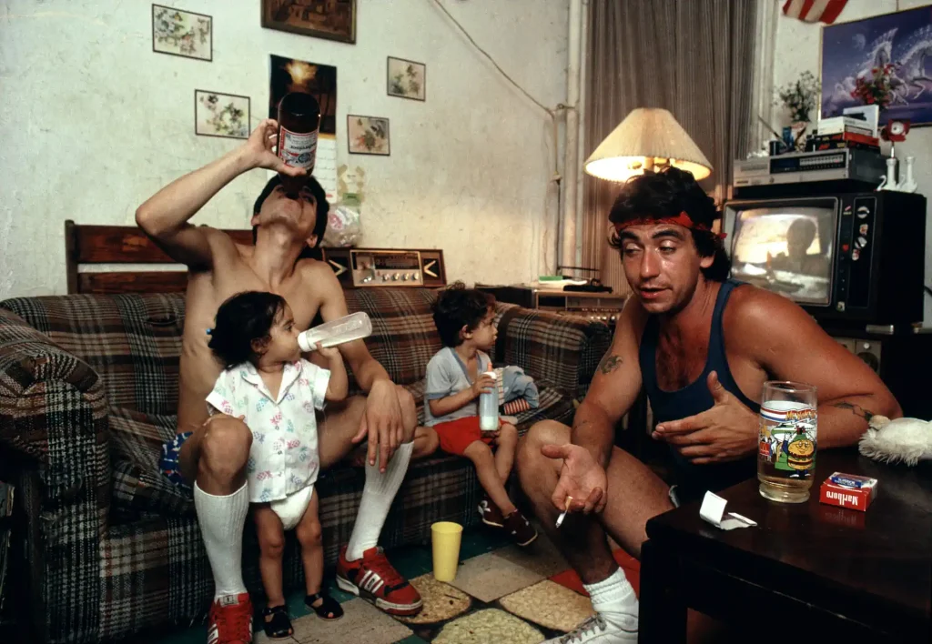 Joseph Rodriguez - Peter drinks a beer with a friend as his children watch TV, Spanish Harlem, NY 1987